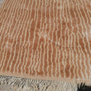 Puede incluir: Una alfombra de rayas marrones y crema con un borde de flecos. La alfombra tiene una textura suave y peluda.