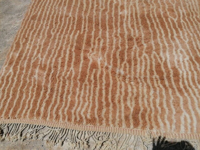 Puede incluir: Una alfombra de rayas marrones y crema con un borde de flecos. La alfombra tiene una textura suave y peluda.