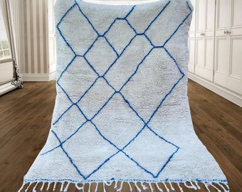 Puede incluir: Alfombra marroquí blanca con un patrón de diamantes azules. La alfombra tiene un borde de flecos.