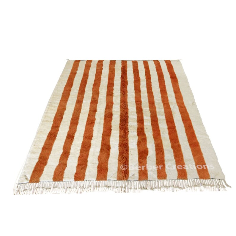 May include: A white and orange striped rug with a fringe border. The rug has a traditional Moroccan design.