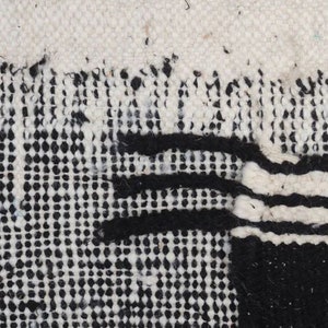 May include: Close-up of a black and white woven rug with a geometric pattern. The rug has a textured surface and is made of natural fibres.