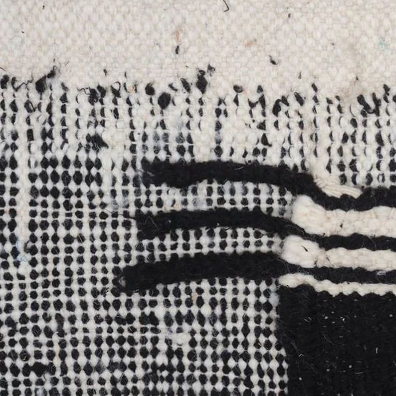 May include: Close-up of a black and white woven rug with a geometric pattern. The rug has a textured surface and is made of natural fibres.