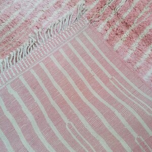 May include: Pink and white striped rug with a fringe border. The rug has a fluffy texture.
