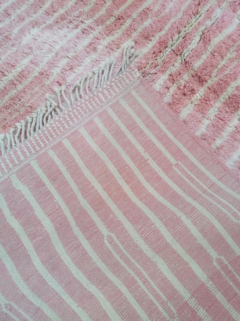 May include: Pink and white striped rug with a fringe border. The rug has a fluffy texture.