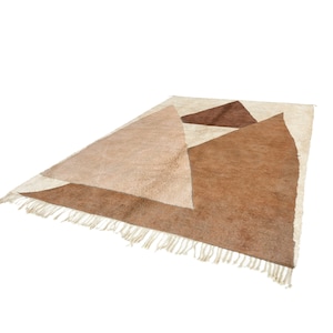 Puede incluir: Una alfombra de color beige y marr&oacute;n con un patr&oacute;n geom&eacute;trico y flecos en los bordes.