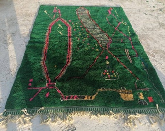 May include: A green rug with a geometric pattern in pink, red, and yellow. The rug has a fringe border.
