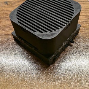 Puede incluir: Un altavoz negro con una rejilla en la parte superior y una base. El altavoz está sobre una superficie de madera.