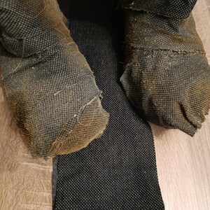 May include: A pair of dark, textured, fabric-covered boots with a worn, brownish-grey appearance and visible frayed edges. The boots feature a dense, woven material construction with a distinct grid-like pattern, showing signs of heavy use and wear.