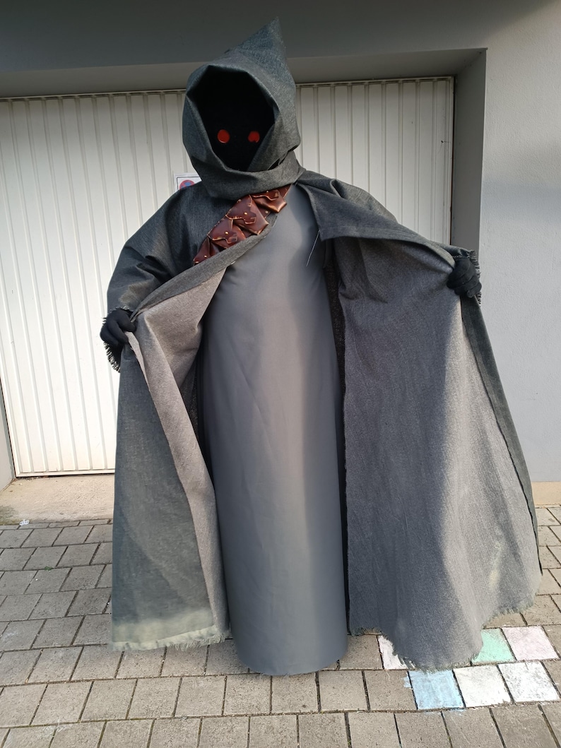 May include: A dark gray hooded cloak worn over a solid gray floor-length tunic. The cloak features a brown leather bandolier with small pouches across the chest. The hood obscures the face, revealing two glowing red circular eyes. Black gloves are worn.