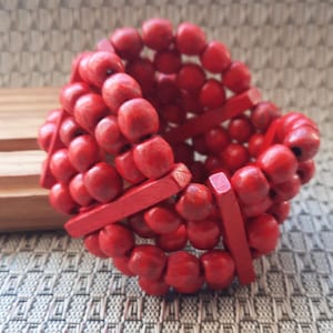 May include: A red wooden beaded bracelet with red wooden spacers. The bracelet is made of multiple strands of beads and is stacked on top of each other.