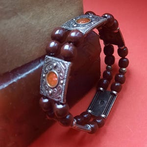 May include: A brown wooden beaded bracelet with silver accents and orange gemstones. The bracelet has two rows of beads and a silver clasp.