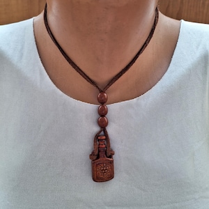 Può includere: Una collana con pendente marrone con un design a bottiglia intagliata e un motivo a uva. La collana ha un cordino marrone e tre perline rotonde. Il pendente è alto circa 4 cm.