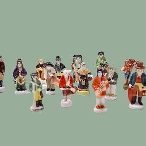 May include: A collection of small, hand-painted ceramic figurines depicting various figures in colorful attire. The figurines stand on small white bases and are arranged against a muted green background. The figures include musicians and other characters.