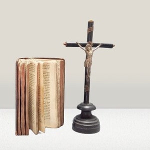 May include: A small, wooden crucifix with a silver figure of Jesus Christ. The crucifix is on a wooden base and is next to a closed book with a brown leather cover.