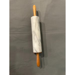 May include: A marble rolling pin with wooden handles. The rolling pin is white with grey veining, and the handles are a light brown colour. This kitchen tool is used for rolling out dough.