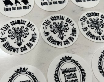 May include: Nine round stickers with black and white designs. The stickers feature a silhouette of a ghost, a quote from the Haunted Mansion ride, and a welcome sign. The quote reads "This chamber has no windows and no doors".
