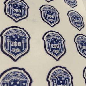 May include: A sheet of white stickers featuring a blue and white crest design. The crest includes the letters "ZOB" and the year "1920", along with stars and other decorative elements. The stickers are arranged in a grid pattern.