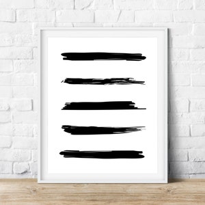 Puede incluir: Una impresión de arte abstracto en blanco y negro con cinco pinceladas horizontales. La impresión está enmarcada en un marco blanco y se muestra sobre una superficie de madera.