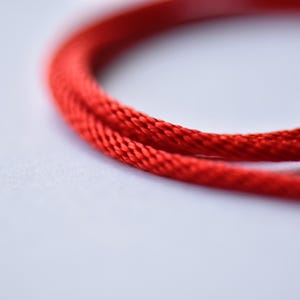 Macro close-up of vibrant red braided silk cord — detailed weave texture showing durability and flexibility for everyday wear.