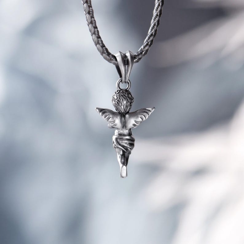 Back view of a silver angel pendant with textured wings and delicate drapery, captured in soft natural light, adding a sense of mystery and ethereal beauty