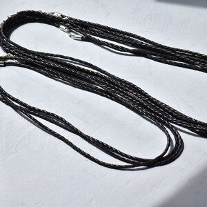 Close-up of multiple black braided leather necklace cords with sterling silver clasps, exuding artisanal charm and effortless elegance