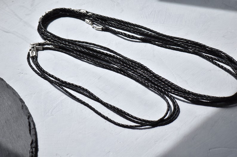 Close-up of multiple black braided leather necklace cords with sterling silver clasps, exuding artisanal charm and effortless elegance