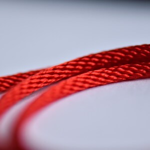 Extreme close-up of red silk cord — shiny braided texture showcasing fine craftsmanship and color intensity.