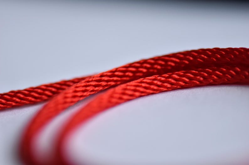 Extreme close-up of red silk cord — shiny braided texture showcasing fine craftsmanship and color intensity.