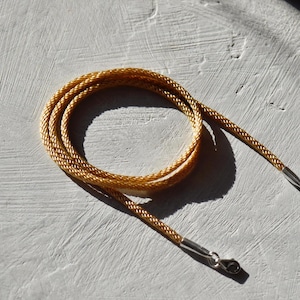 Peut inclure: Un collier en cordon doré avec des fermoirs argentés. Le cordon est tressé et a un léger éclat.