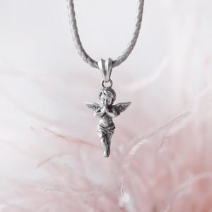 Romantic silver angel pendant with finely detailed wings and praying pose, highlighted against a dreamy feather background, perfect for heartfelt gifting