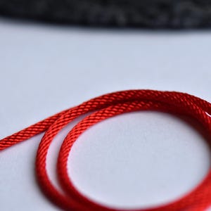 Vibrant red braided silk cord coiled on white background — close-up shows fine texture and rich color for minimalist jewelry styling.