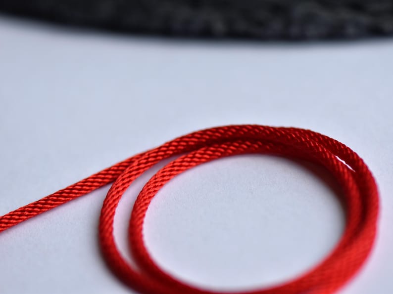 Vibrant red braided silk cord coiled on white background — close-up shows fine texture and rich color for minimalist jewelry styling.