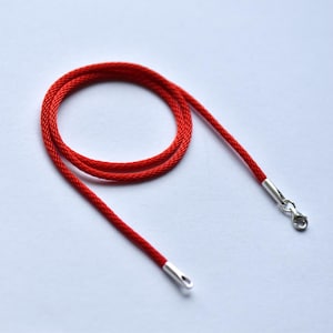 Minimalist flat lay of a red braided silk cord with 925 silver clasp — vibrant color meets clean design for modern jewelry lovers.