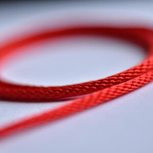 Close-up of red silk necklace cord — braided texture and vivid shine captured in soft focus for a luxurious and tactile impression.