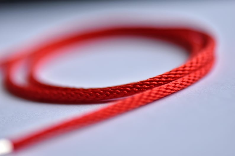 Close-up of red silk necklace cord — braided texture and vivid shine captured in soft focus for a luxurious and tactile impression.
