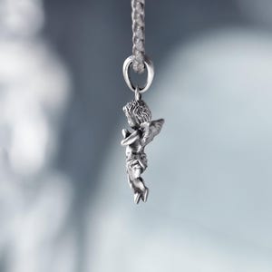 Side view of a silver angel pendant with flowing hair and delicate wings, softly illuminated to highlight its romantic details and ethereal charm