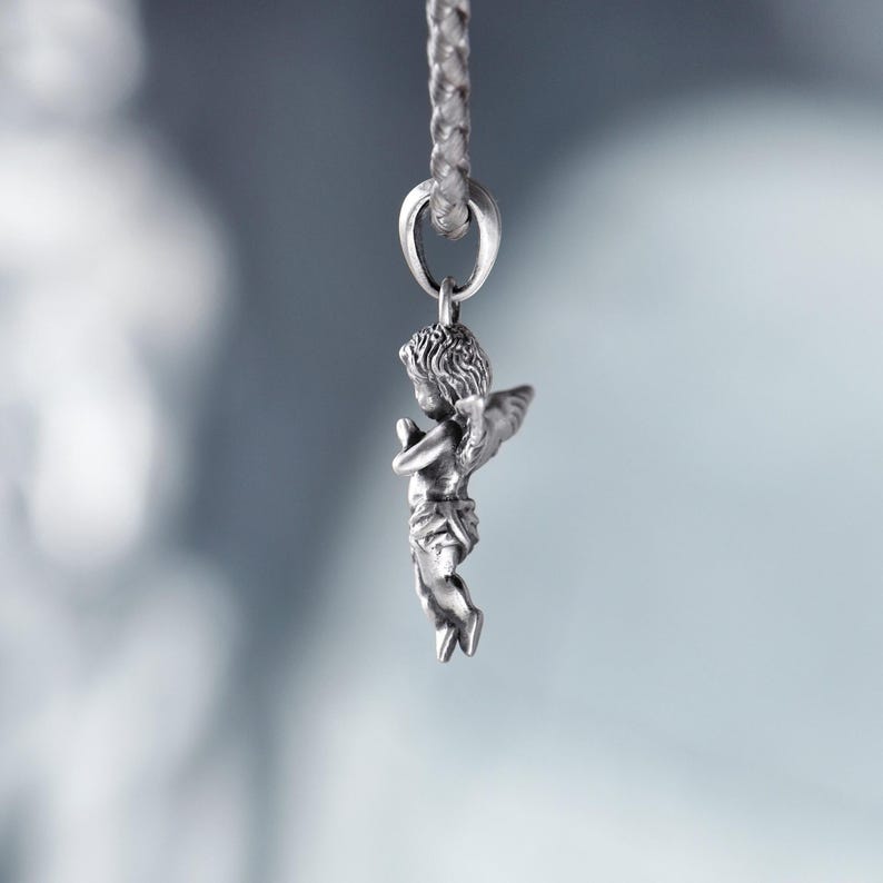 Side view of a silver angel pendant with flowing hair and delicate wings, softly illuminated to highlight its romantic details and ethereal charm