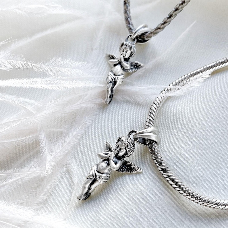 A pair of guardian angel pendants resting on white satin with wispy feathers, radiating a protective and peaceful aura