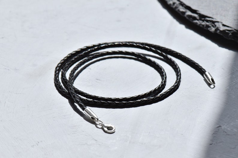 Detailed texture of a black braided leather necklace cord with a shimmering silver clasp, exuding sophistication and versatility for your jewelry collection
