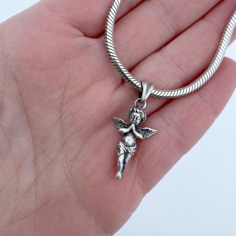 Graceful silver angel charm pendant, showcased in a hand, highlighting the fine craftsmanship and spiritual significance of the jewelry piece