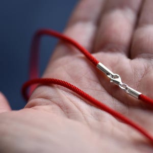Hand holding a red braided silk cord with sterling silver clasp — vibrant color meets artisan texture, ideal for pendants or minimalist layering necklaces.