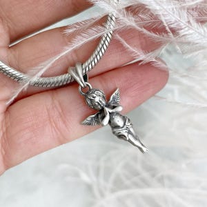 Close-up of a silver angel charm in prayer, held tenderly in hand, framed by soft white feathers that highlight its serene elegance and protective symbolism