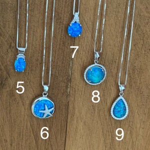May include: Nine silver necklaces with blue opal pendants. The pendants feature different designs, including a teardrop, a circle with a starfish, and a circle with a starburst.