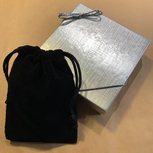 May include: A black velvet drawstring pouch with a silver gift box with a silver bow on top.