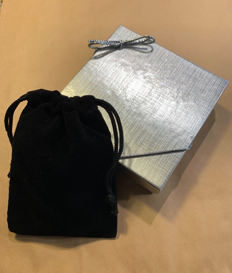 May include: A black velvet drawstring pouch with a silver gift box with a silver bow on top.