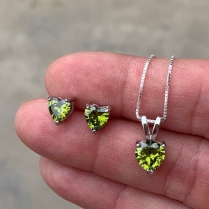 May include: A set of green heart-shaped earrings and a matching pendant necklace. The jewelry is made of silver and features a sparkling green stone.