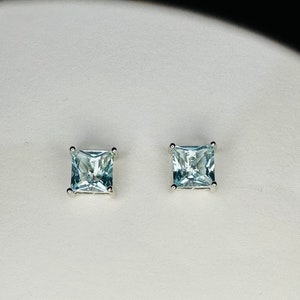 May include: A pair of silver square stud earrings with light blue aquamarine gemstones.