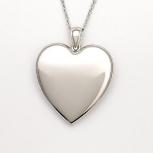 May include: A silver heart pendant necklace. The pendant is a polished heart shape, suspended from a fine chain. The necklace is shown against a white backdrop, emphasising its reflective surface and simple design.
