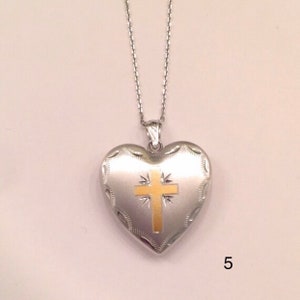 May include: A silver heart-shaped locket with a gold cross design on the front. The locket is attached to a silver chain.