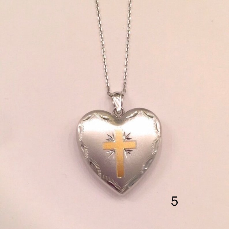 May include: A silver heart-shaped locket with a gold cross design on the front. The locket is attached to a silver chain.